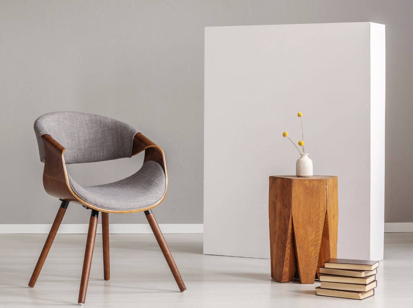 A grey upholstered chair beside a wooden side table with a small vase of flowers